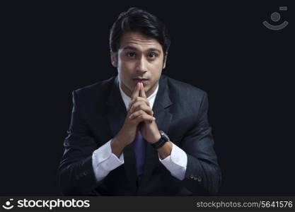 Portrait of confident businessman sitting with hands clasped against black background