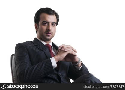 Portrait of confident businessman sitting with hands clasped against white background