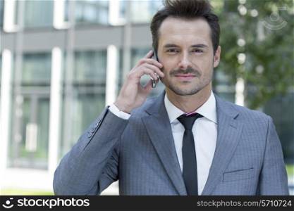 Portrait of confident businessman using cell phone outside office