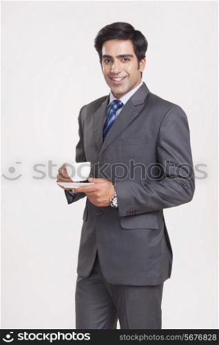 Portrait of confident businessman with coffee cup over gray background