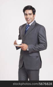 Portrait of confident businessman with coffee cup over gray background