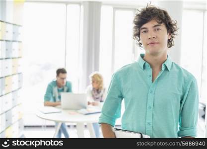 Portrait of confident businessman with colleagues working in background at creative office