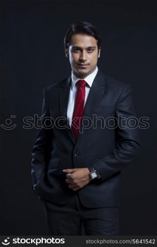 Portrait of confident businessman with hand in pocket over black background