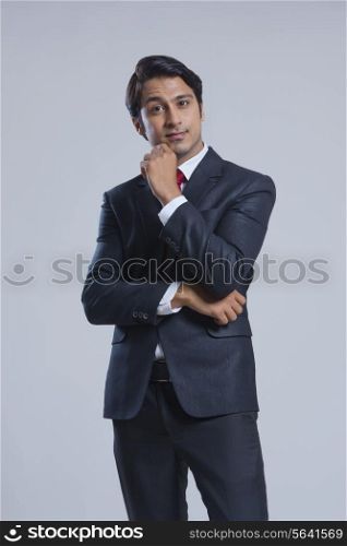 Portrait of confident businessman with hand on chin against gray background
