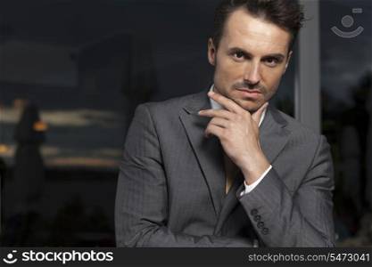 Portrait of confident businessman with hand on chin in office