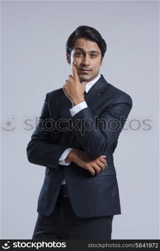 Portrait of confident businessman with hand on chin over gray background