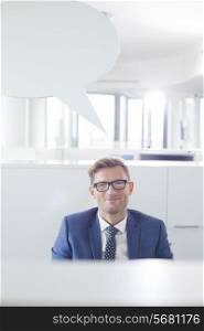 Portrait of confident businessman with speech bubble in office