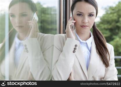 Portrait of confident businesswoman answering cell phone by glass door