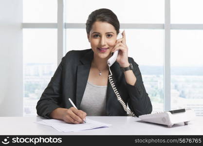 Portrait of confident businesswoman answering telephone at office desk