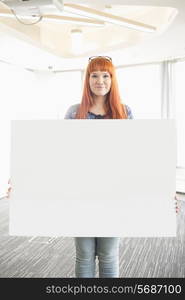 Portrait of confident businesswoman holding blank placard in creative office