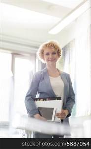 Portrait of confident businesswoman holding files in creative office
