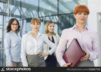 Portrait of confident businesswoman holding folder with female colleagues standing in background