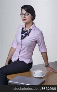 Portrait of confident businesswoman sitting on office desk