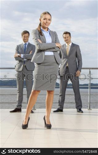 Portrait of confident businesswoman standing with coworkers on terrace against sky