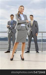 Portrait of confident businesswoman standing with coworkers on terrace against sky