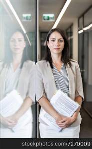 Portrait of confident businesswoman standing with documents at office