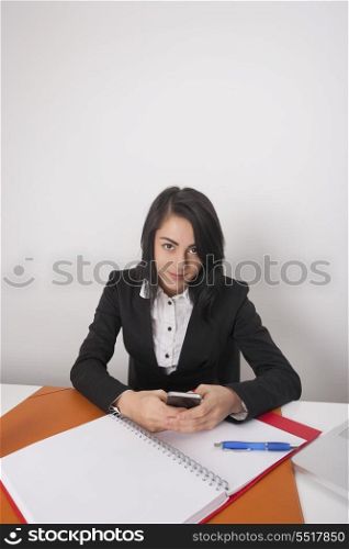 Portrait of confident businesswoman with cell phone sitting at office desk