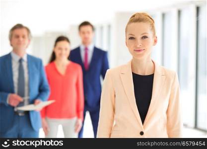 Portrait of confident businesswoman with colleagues in background at office