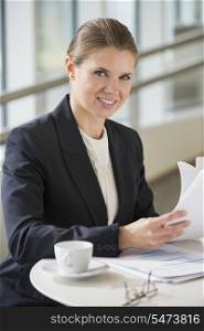 Portrait of confident businesswoman with documents sitting at office cafe