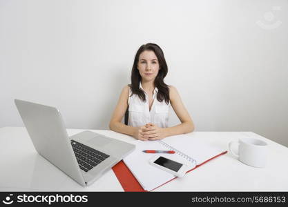 Portrait of confident businesswoman with laptop and binder at desk in office