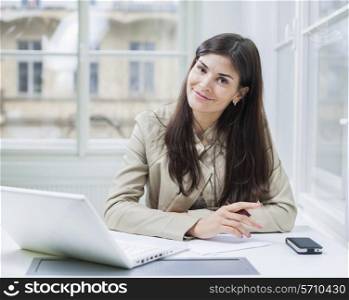 Portrait of confident businesswoman with laptop sitting at office desk