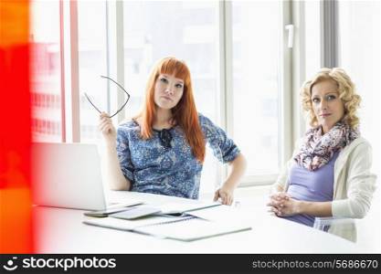 Portrait of confident creative businesswomen sitting at desk in office
