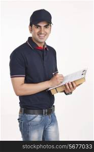 Portrait of confident delivery man with clipboard and package against white background