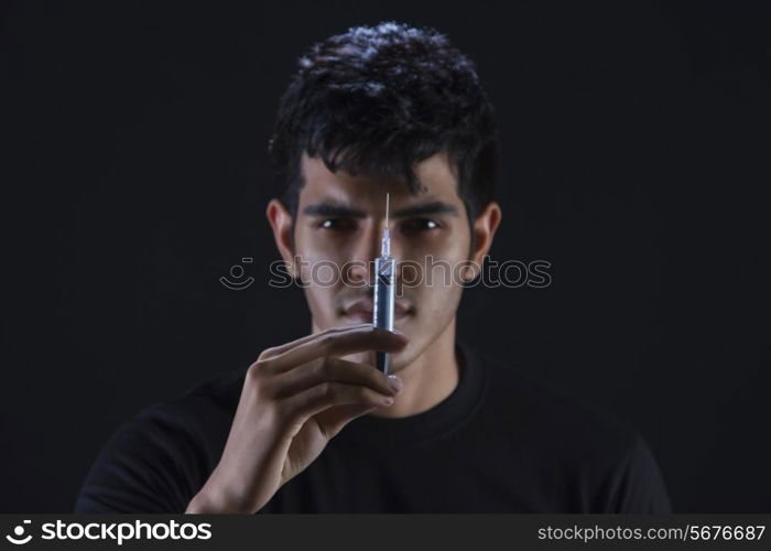 Portrait of confident drug addict holding syringe against black background