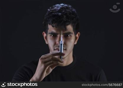 Portrait of confident drug addict holding syringe against black background