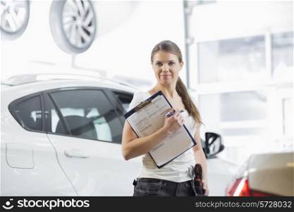 Portrait of confident female mechanic with clipboard in car workshop