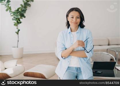 Portrait of confident freelancer, entrepreneur or businesswoman, which leans to the workstation. Young hispanic woman is working at home. Remote work online on quarantine. Home office interior.. Portrait of confident freelancer or businesswoman, which leans to the workstation at home office.