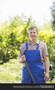 Portrait of confident gardener holding rake in plant nursery