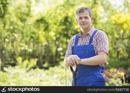 Portrait of confident gardener holding spade in plant nursery