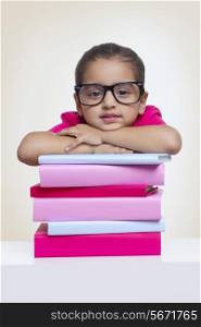 Portrait of confident girl leaning on stack of books against colored background