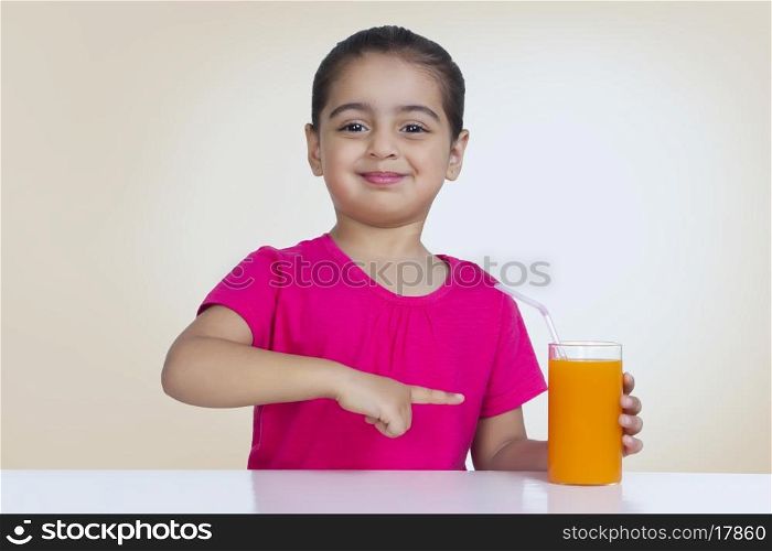 Portrait of confident girl showing orange juice against colored background