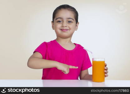 Portrait of confident girl showing orange juice against colored background