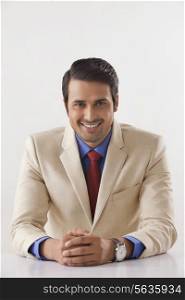 Portrait of confident Indian businessman in suit sitting at office desk