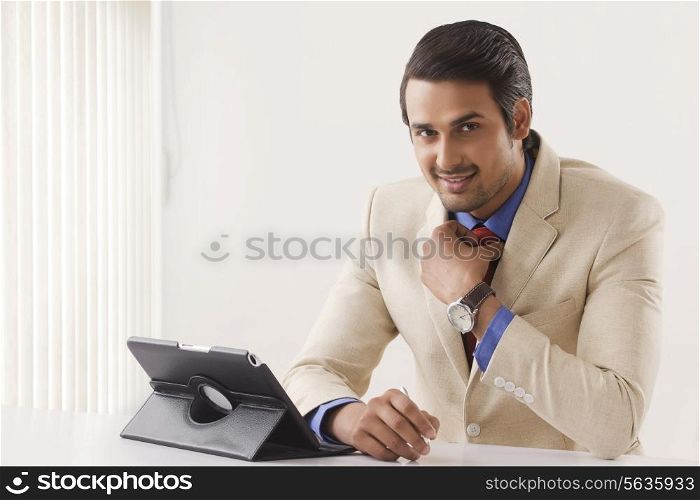 Portrait of confident Indian businessman with digital tablet at office desk