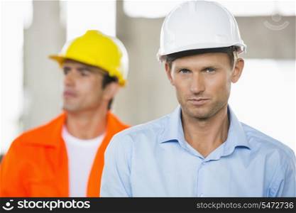 Portrait of confident male architect at construction site with coworker in background