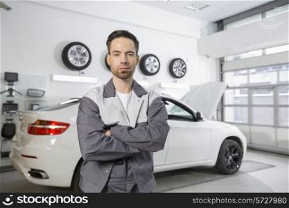 Portrait of confident male automobile mechanic standing in front of car at workshop