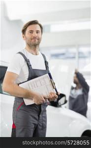 Portrait of confident male automobile mechanic with clipboard in car repair store