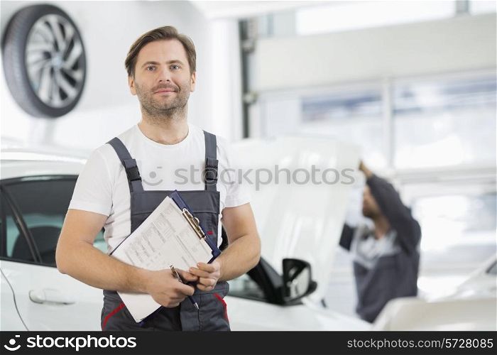 Portrait of confident male maintenance engineer with clipboard in car repair shop