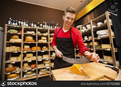 Portrait of confident male salesperson cutting cheese in store