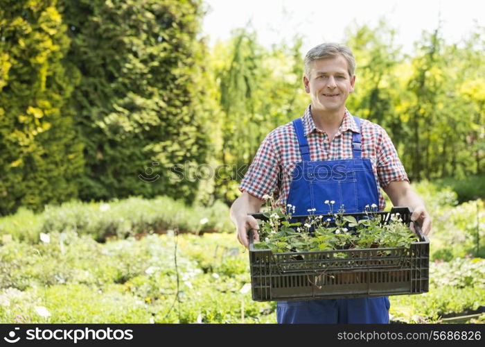 Portrait of confident man holding crate of potted plants at garden