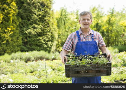 Portrait of confident man holding crate of potted plants at garden
