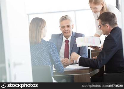 Portrait of confident mature businessman with colleagues in meeting room