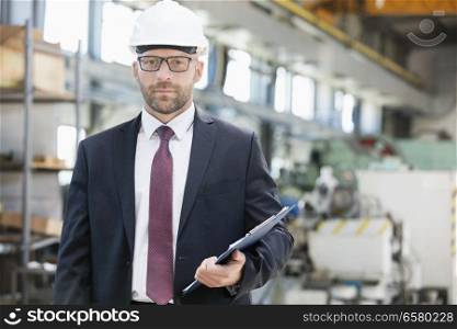Portrait of confident mid adult male supervisor holding clipboard in metal industry
