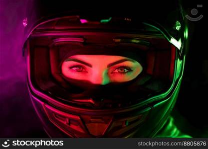 Portrait of confident motorcyclist woman in closed motorcycle helmet. Young driver biker looking to camera under pink and green neon colorful light at night. High quality photo. Portrait of confident motorcyclist woman in closed motorcycle helmet. Young driver biker looking to camera under pink and green neon colorful light at night.