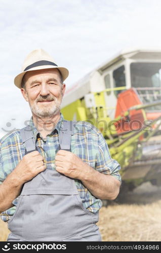 Portrait of confident senior farmer standing against tractor at farm