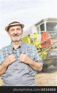 Portrait of confident senior farmer standing against tractor at farm